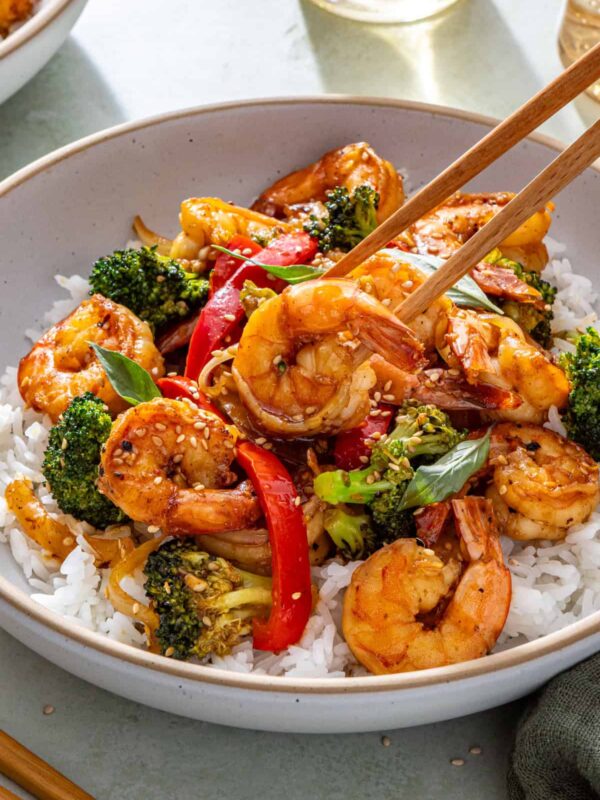 Easy shrimp stir fry served over rice with chopsticks lifting shrimp from bowl