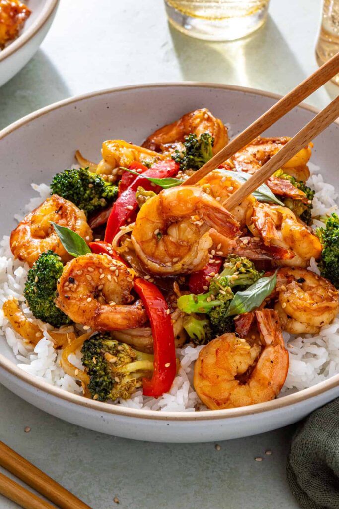 Easy shrimp stir fry served over rice with chopsticks lifting shrimp from bowl