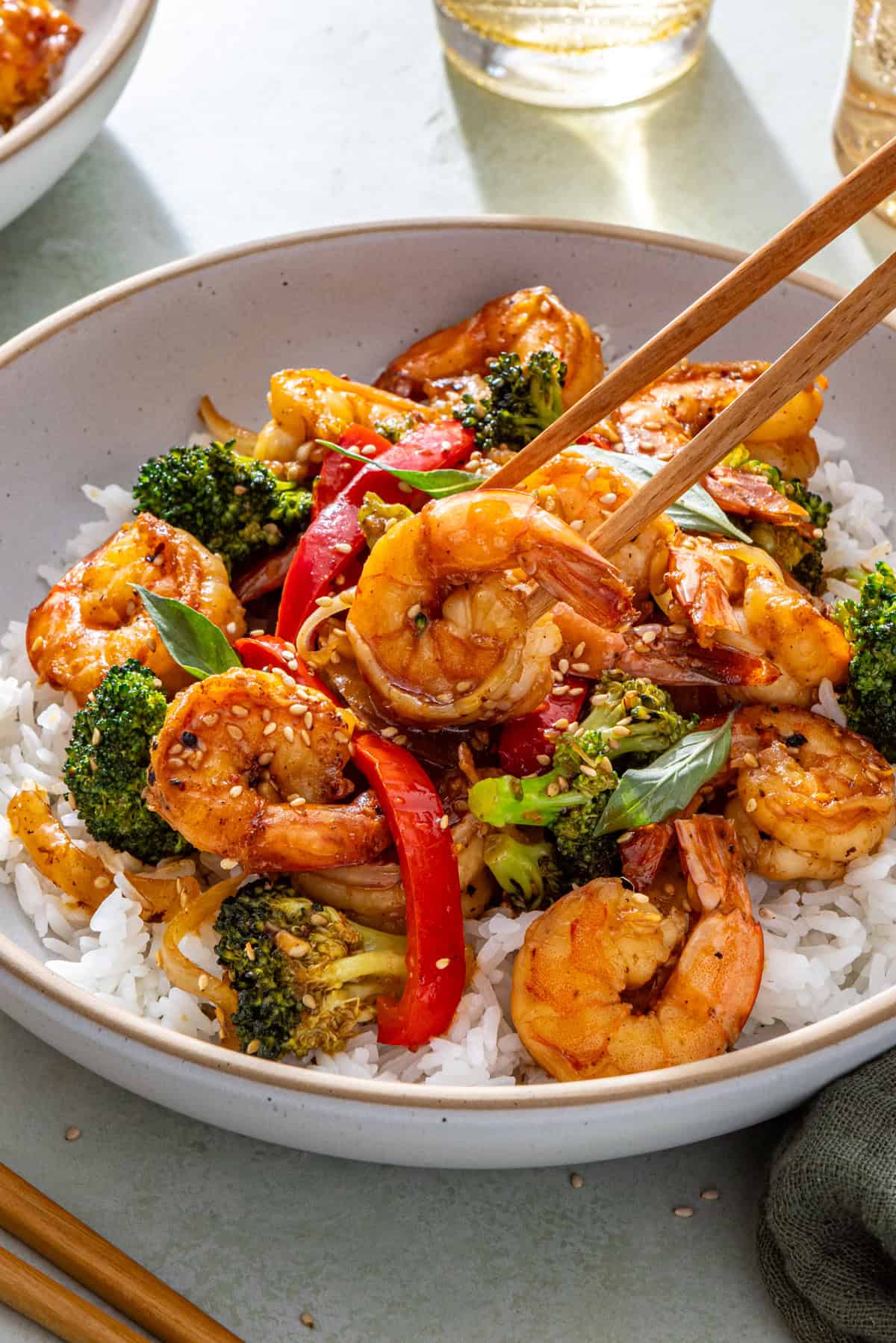 Easy shrimp stir fry served over rice with chopsticks lifting shrimp from bowl