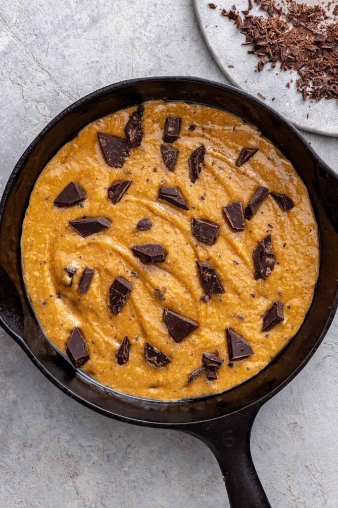 Chocolate chip cookie skillet dough pressed into cast iron skillet with extra chocolate on top