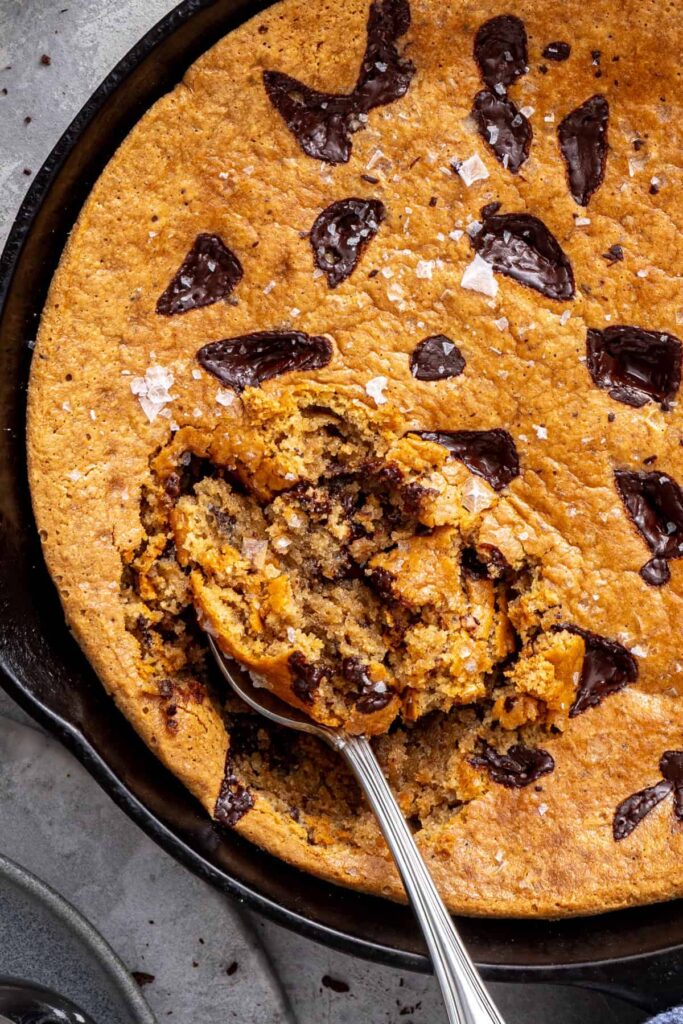 Overhead shot of healthy chocolate chip cookie skillet with flaky sea salt being scooped to serve