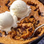 Healthy chocolate chip cookie skillet with melting dairy-free vanilla ice cream and a spoon scooping into the center