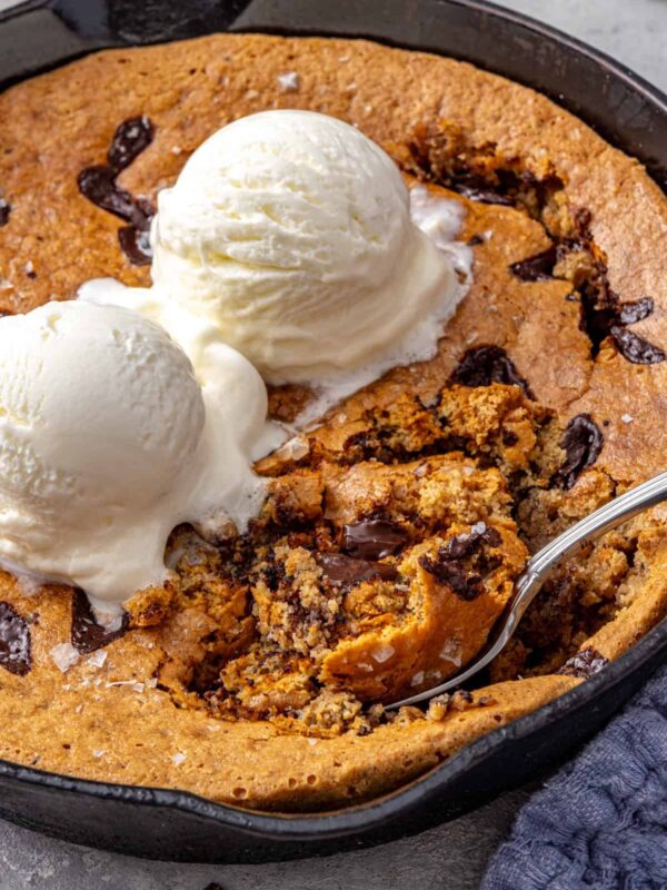 Healthy chocolate chip cookie skillet with melting dairy-free vanilla ice cream and a spoon scooping into the center