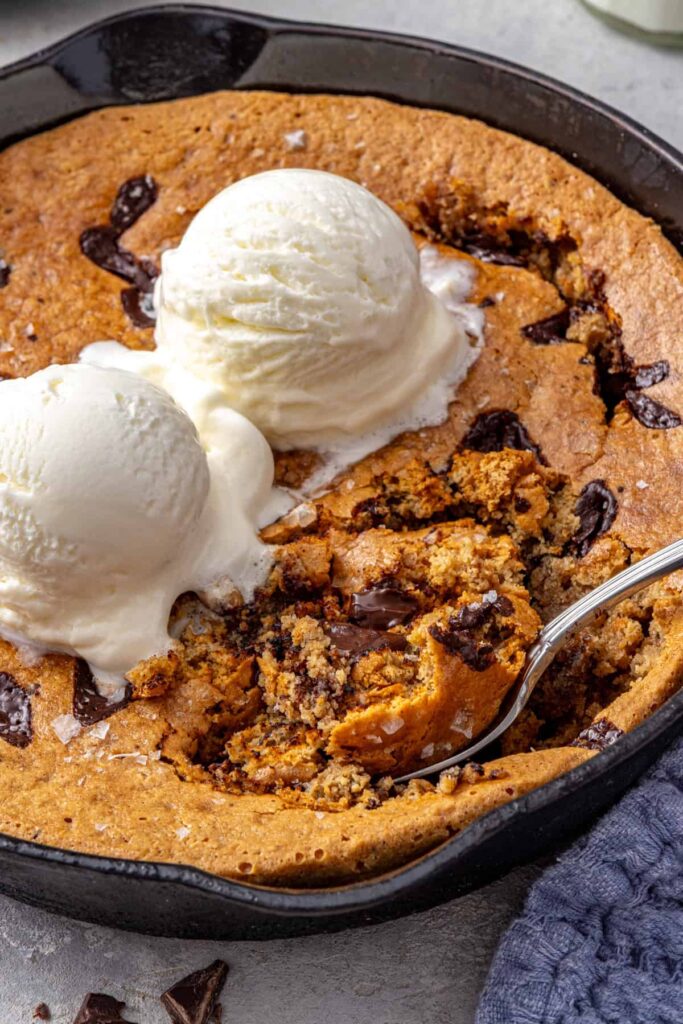 Healthy chocolate chip cookie skillet with melting dairy-free vanilla ice cream and a spoon scooping into the center