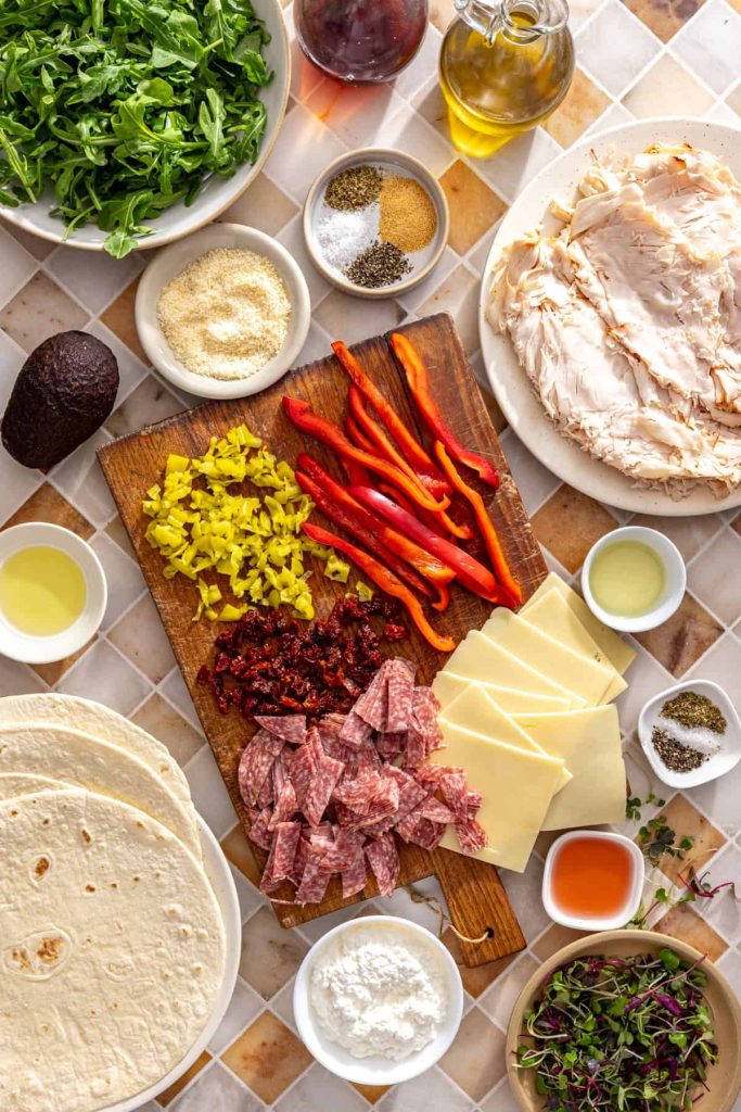 Ingredients for high-protein turkey pinwheels including turkey, cottage cheese, arugula, avocado, salami, and cassava tortillas