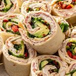 High-protein turkey pinwheels with cottage cheese spread, turkey, salami, avocado, and greens on a serving platter