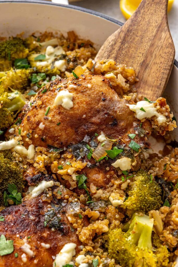 Wooden spatula serving lemon herb chicken quinoa pilaf from skillet