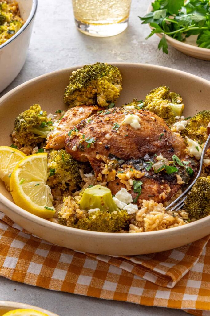 Lemon herb chicken quinoa pilaf served in a shallow bowl with lemon wedges and a fork on a styled table