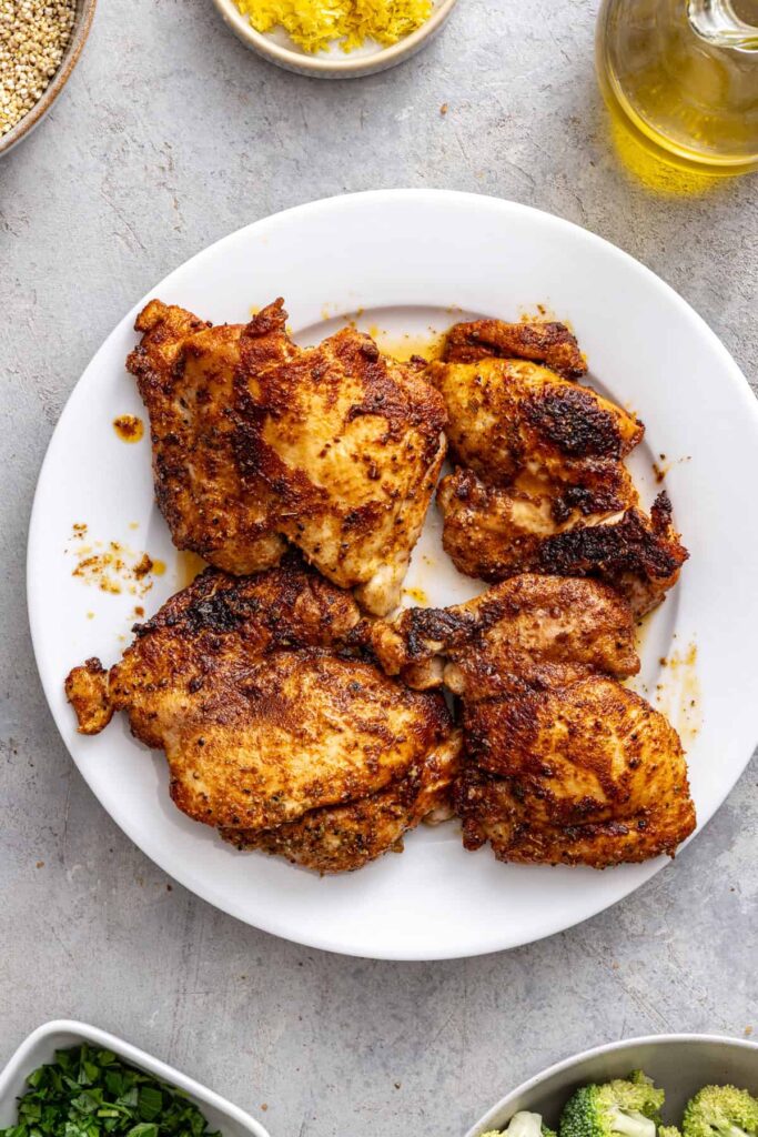 cooked chicken thighs set aside on a plate before adding back to skillet to make pilaf