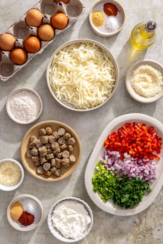 Overhead shot of ingredients for gluten-free quiche cups including eggs, cottage cheese, shredded potatoes, vegetables, and spices arranged on a kitchen counter
