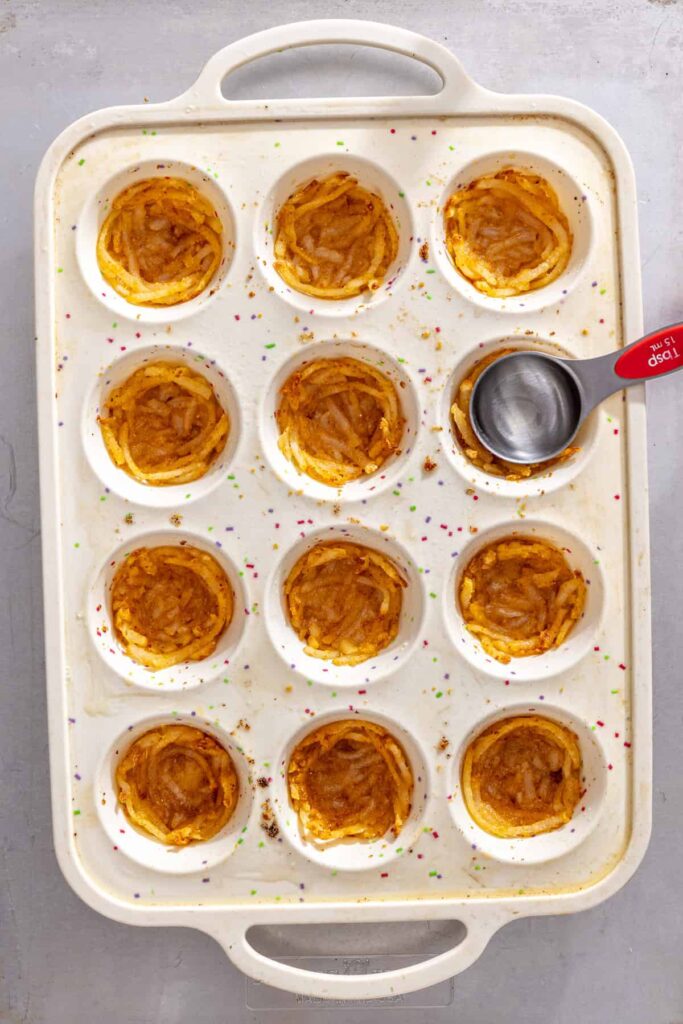 Pressing seasoned shredded potato mixture into silicone muffin tin for gluten-free quiche cups crust