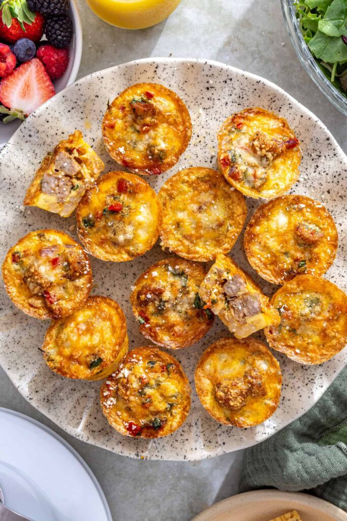 Styled gluten-free quiche cups on cake stand with breakfast spread and fresh fruit