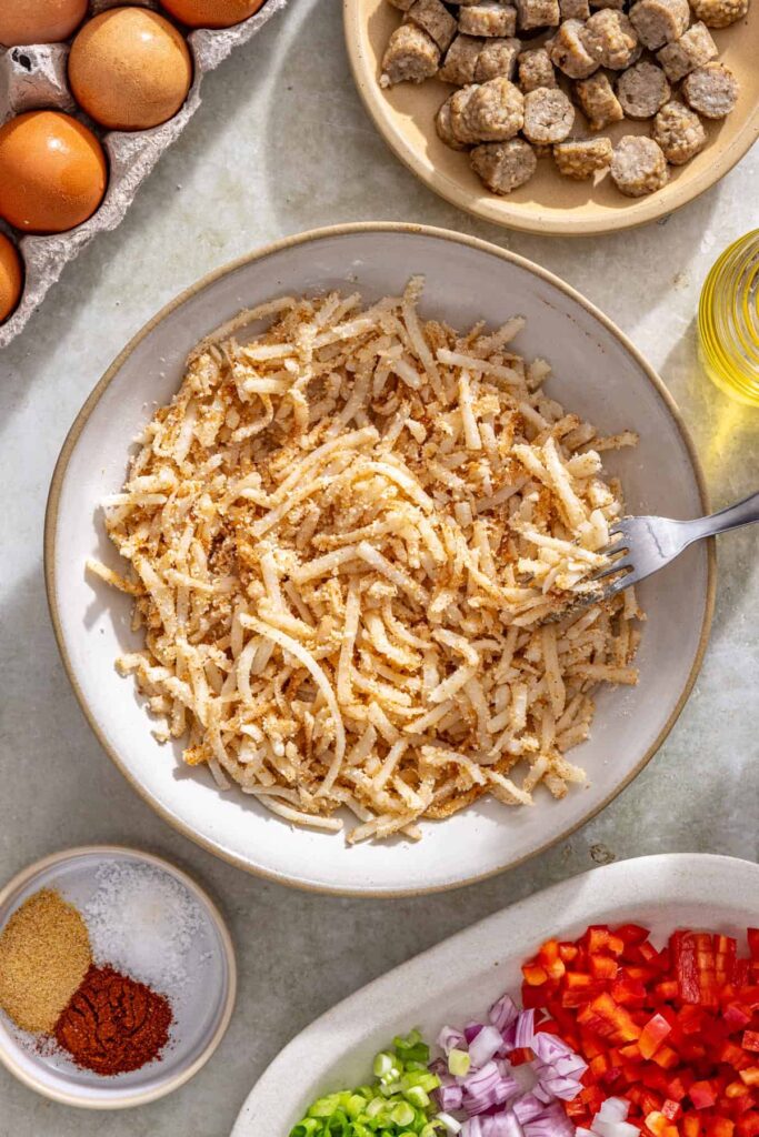 Tossing shredded potatoes with seasoning and parmesan to form the crust for gluten-free quiche cups