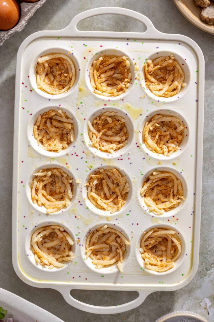 Forming the base layer of mini gluten-free quiche cups using shredded potatoes in a silicone mold