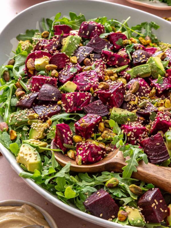 Roasted beet salad with goat cheese, avocado, arugula, pistachios, and tahini dressing served in a platter with a serving spoon on a styled table