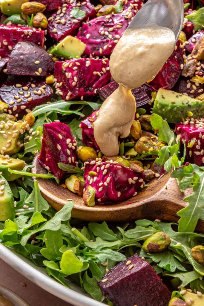 close-up of Tahini dressing being drizzled over roasted beet salad