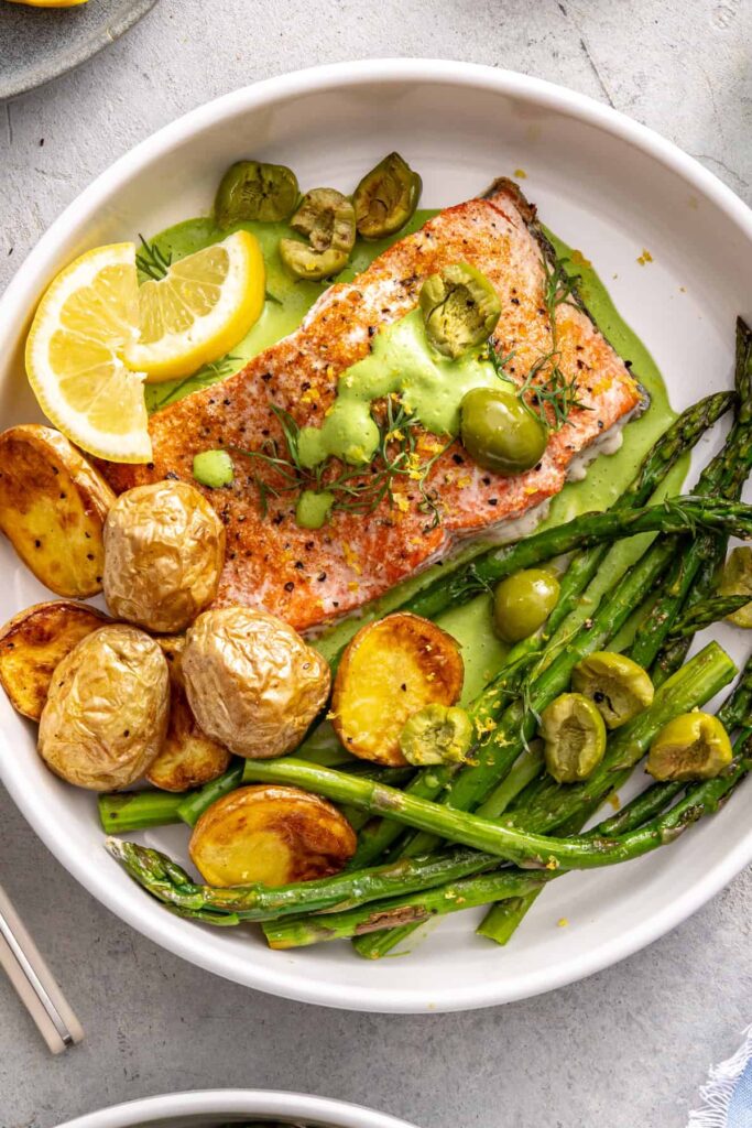 Baked salmon served with asparagus, herb sauce, potatoes, and olives