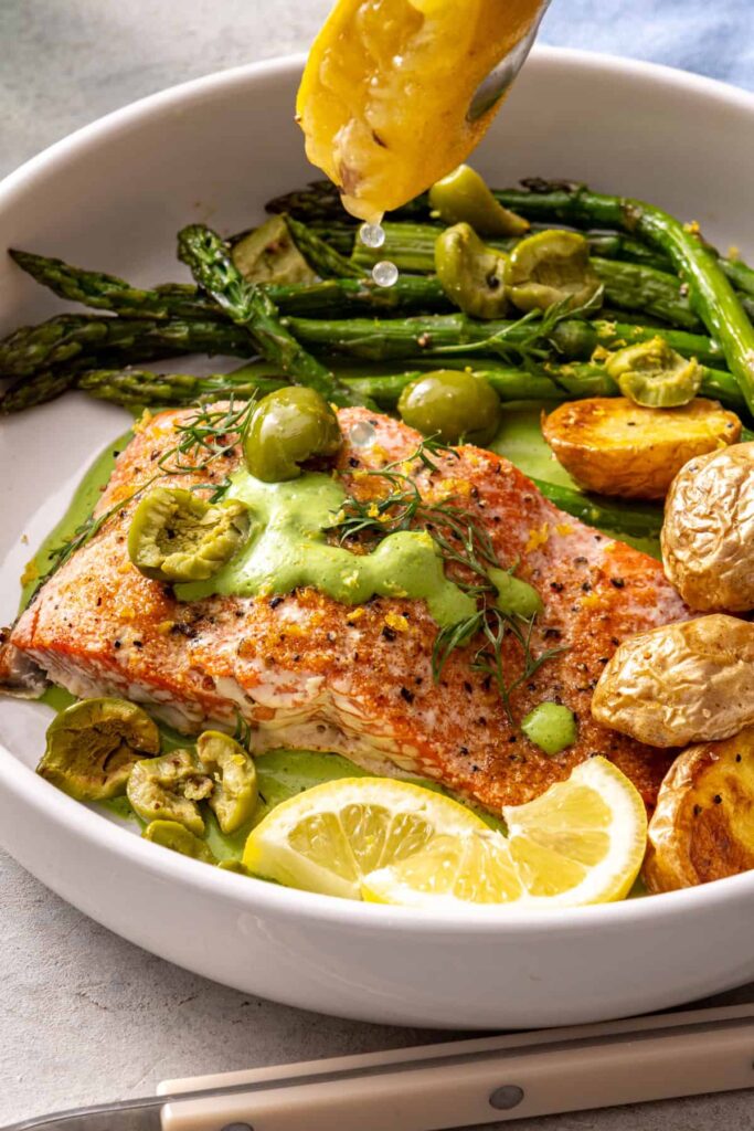 Roasted lemon being squeezed over baked salmon and asparagus