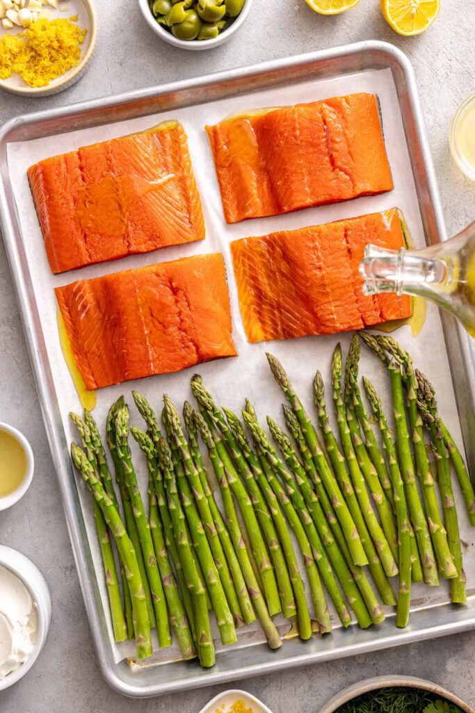 Olive oil being drizzled over salmon and asparagus on sheet pan