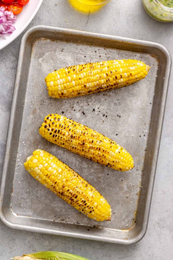Charred grilled corn cooling before being added to corn and tomato salad