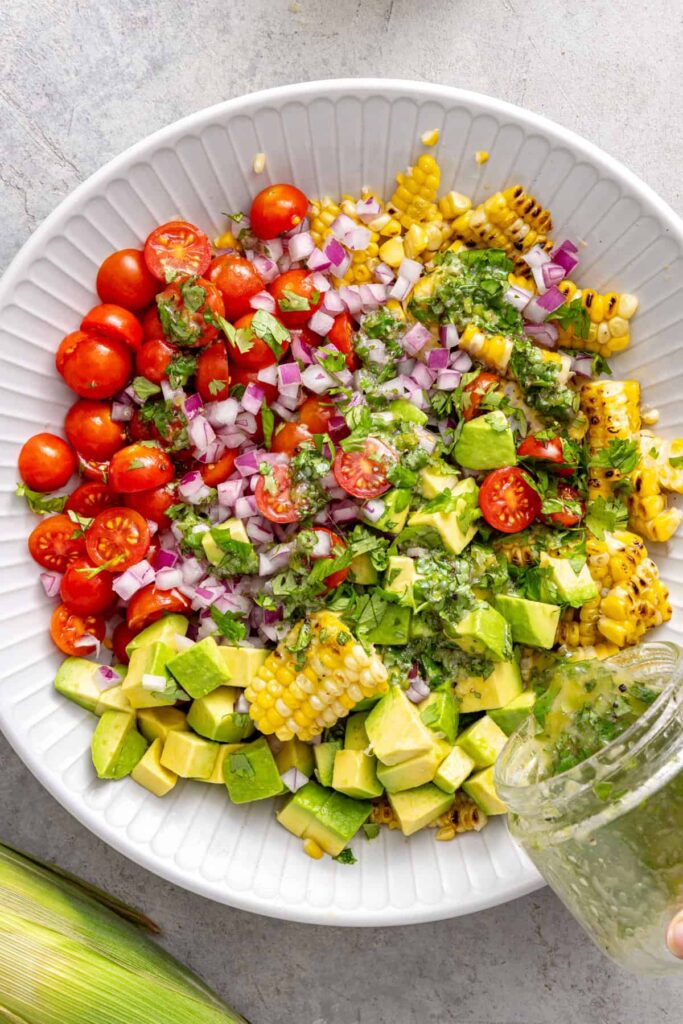 Charred corn, tomatoes, avocado, red onion, and cilantro in a mixing bowl