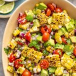 Corn and tomato salad with charred corn, avocado, and cilantro lime dressing served on a colorful summer table with fresh lime wedges