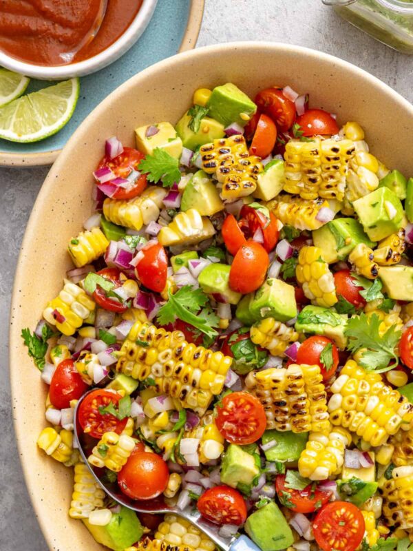 Corn and tomato salad with charred corn, avocado, and cilantro lime dressing served on a colorful summer table with fresh lime wedges