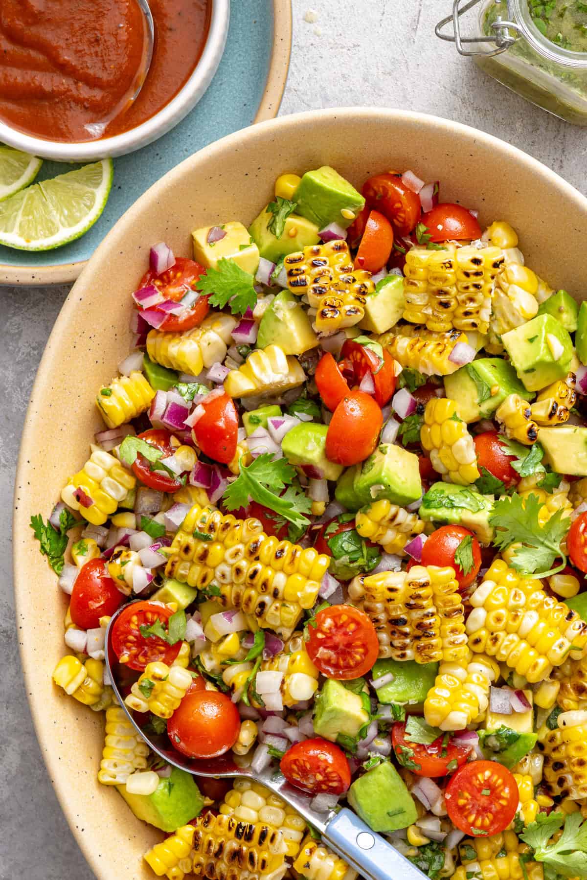Corn and tomato salad with charred corn, avocado, and cilantro lime dressing served on a colorful summer table with fresh lime wedges