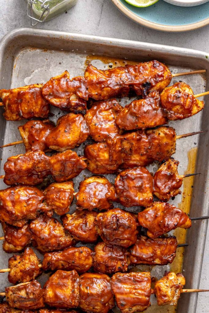 Overhead view of a sheet pan filled with grilled BBQ chicken skewers