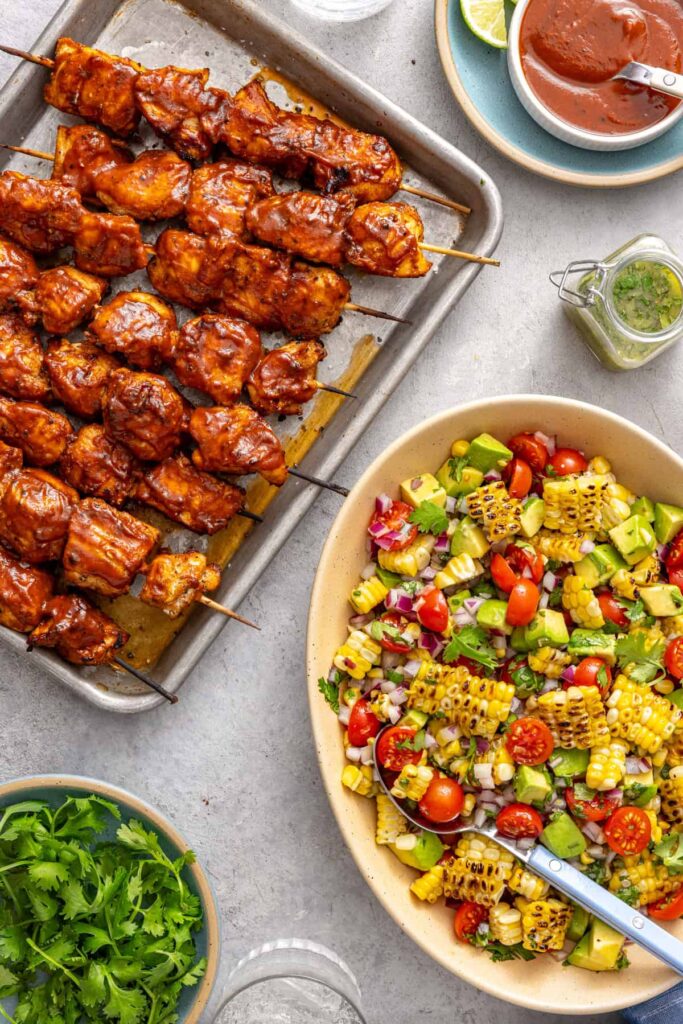 BBQ chicken skewers served with corn and tomato summer salad on a styled table