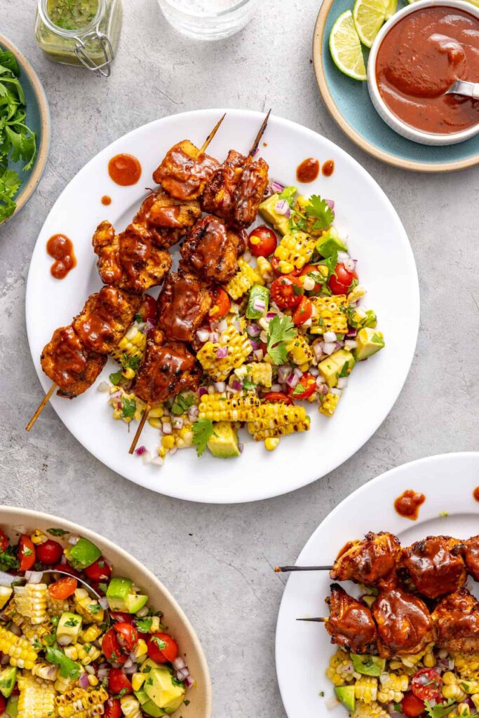 Healthy BBQ chicken skewers served with corn and tomato summer salad