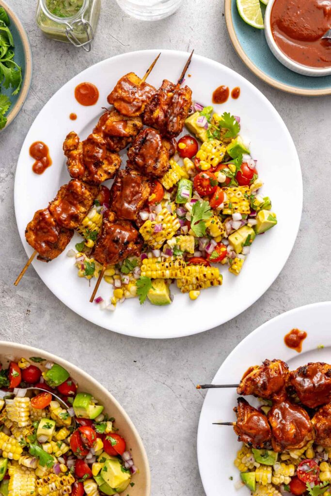 BBQ chicken skewers plated with fresh summer salad and BBQ sauce
