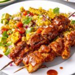 Healthy BBQ chicken skewers served with corn and tomato summer salad on a dinner plate