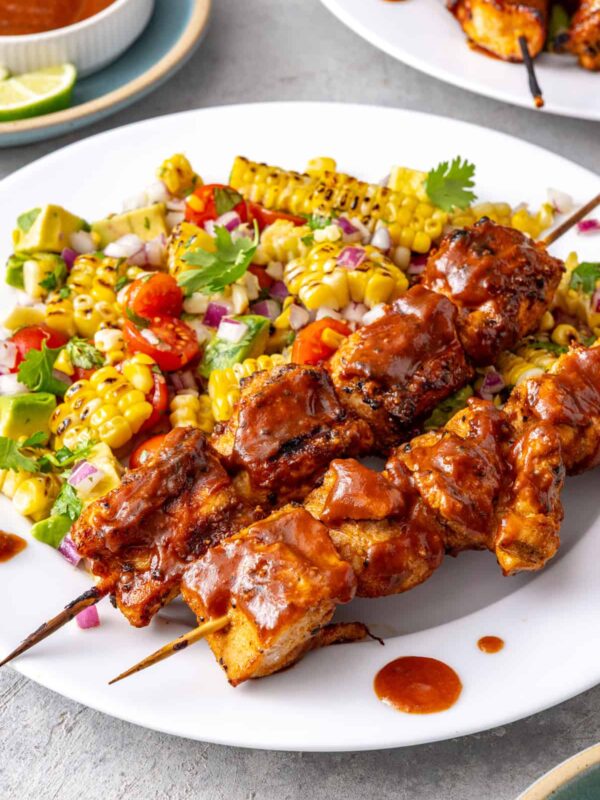 Healthy BBQ chicken skewers served with corn and tomato summer salad on a dinner plate