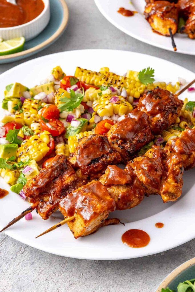 Healthy BBQ chicken skewers served with corn and tomato summer salad on a dinner plate