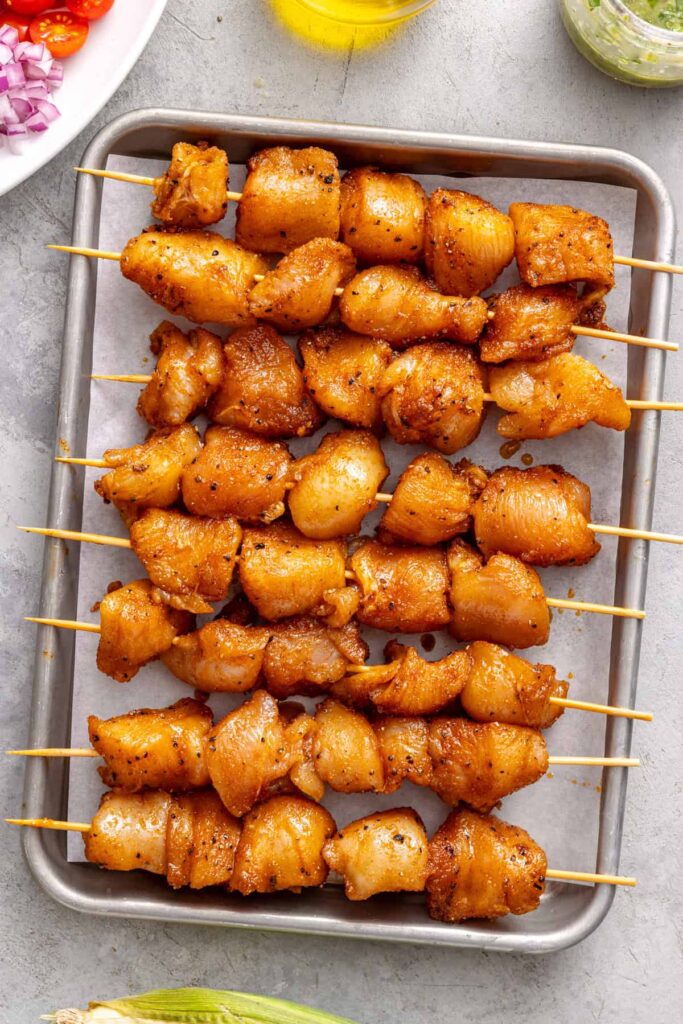 Raw seasoned chicken arranged on skewers before grilling