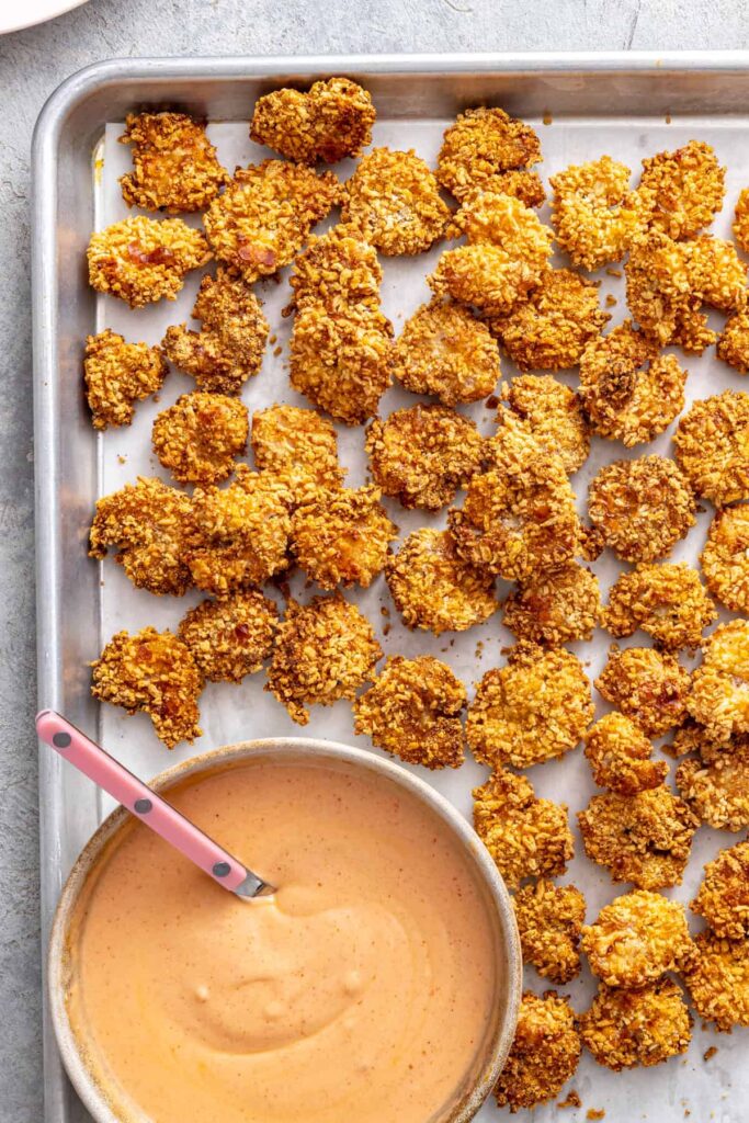 Golden crispy air fryer bang bang shrimp cooling on a baking sheet beside homemade bang bang sauce