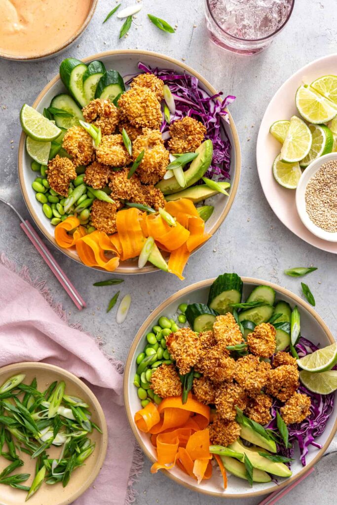 Overhead view of healthy air fryer bang bang shrimp bowls with rice, vegetables, lime wedges and sesame seeds.