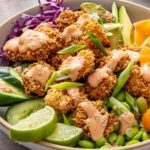 Healthy air fryer bang bang shrimp bowl with crispy gluten-free shrimp, rice, fresh vegetables, avocado, lime wedges and creamy dairy-free bang bang sauce.