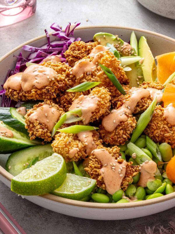 Healthy air fryer bang bang shrimp bowl with crispy gluten-free shrimp, rice, fresh vegetables, avocado, lime wedges and creamy dairy-free bang bang sauce.