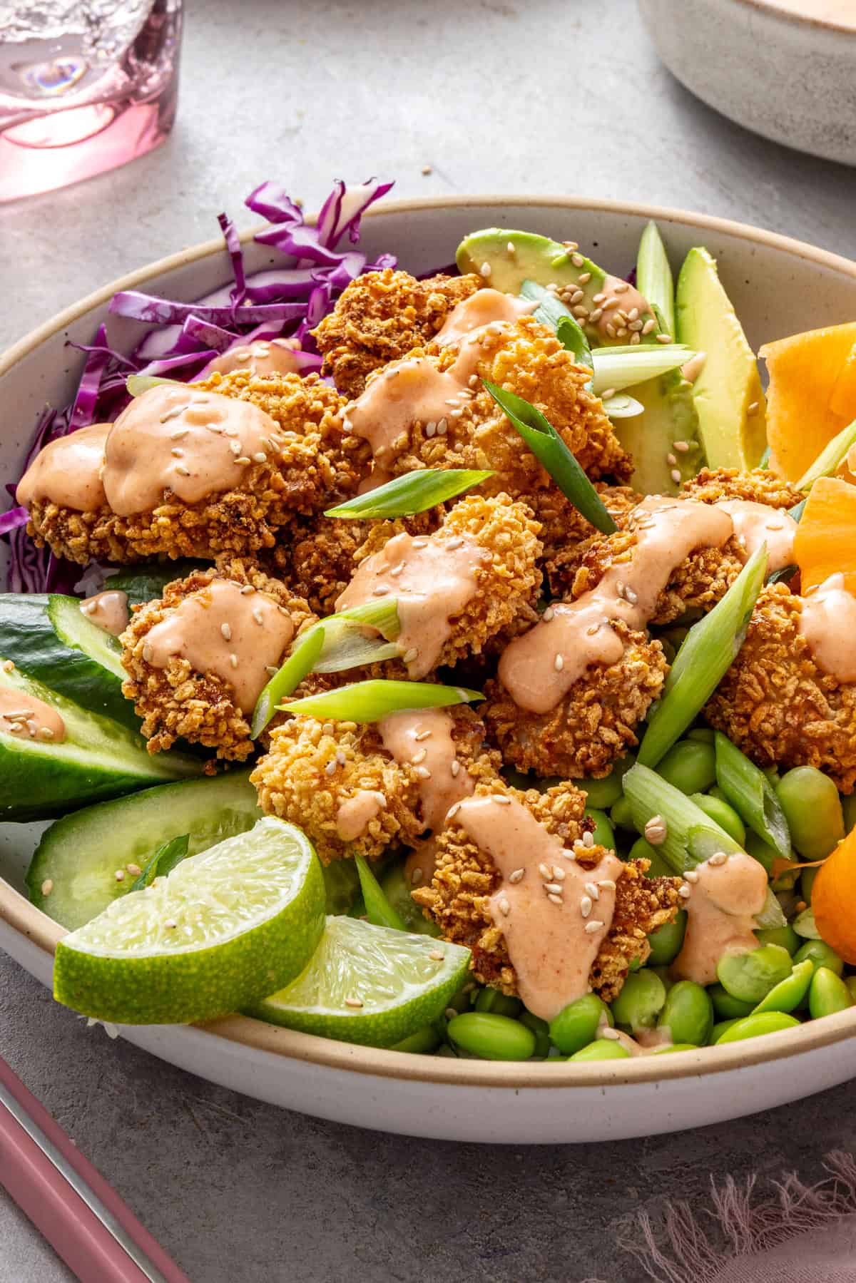 Healthy air fryer bang bang shrimp bowl with crispy gluten-free shrimp, rice, fresh vegetables, avocado, lime wedges and creamy dairy-free bang bang sauce.