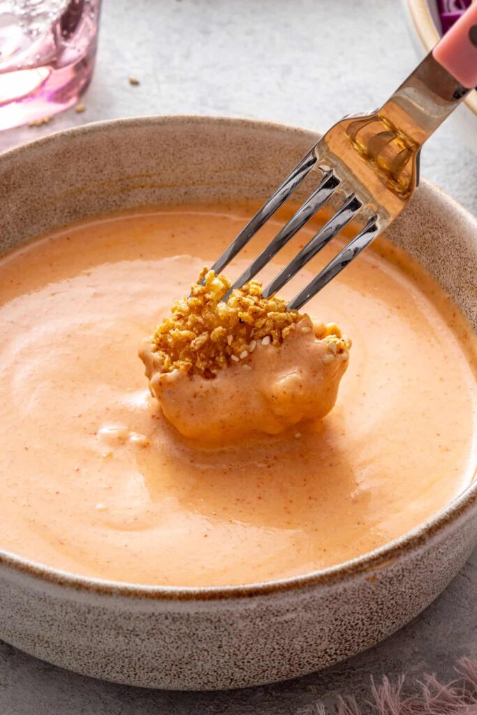 Fork dipping crispy air fryer bang bang shrimp into creamy homemade bang bang sauce.