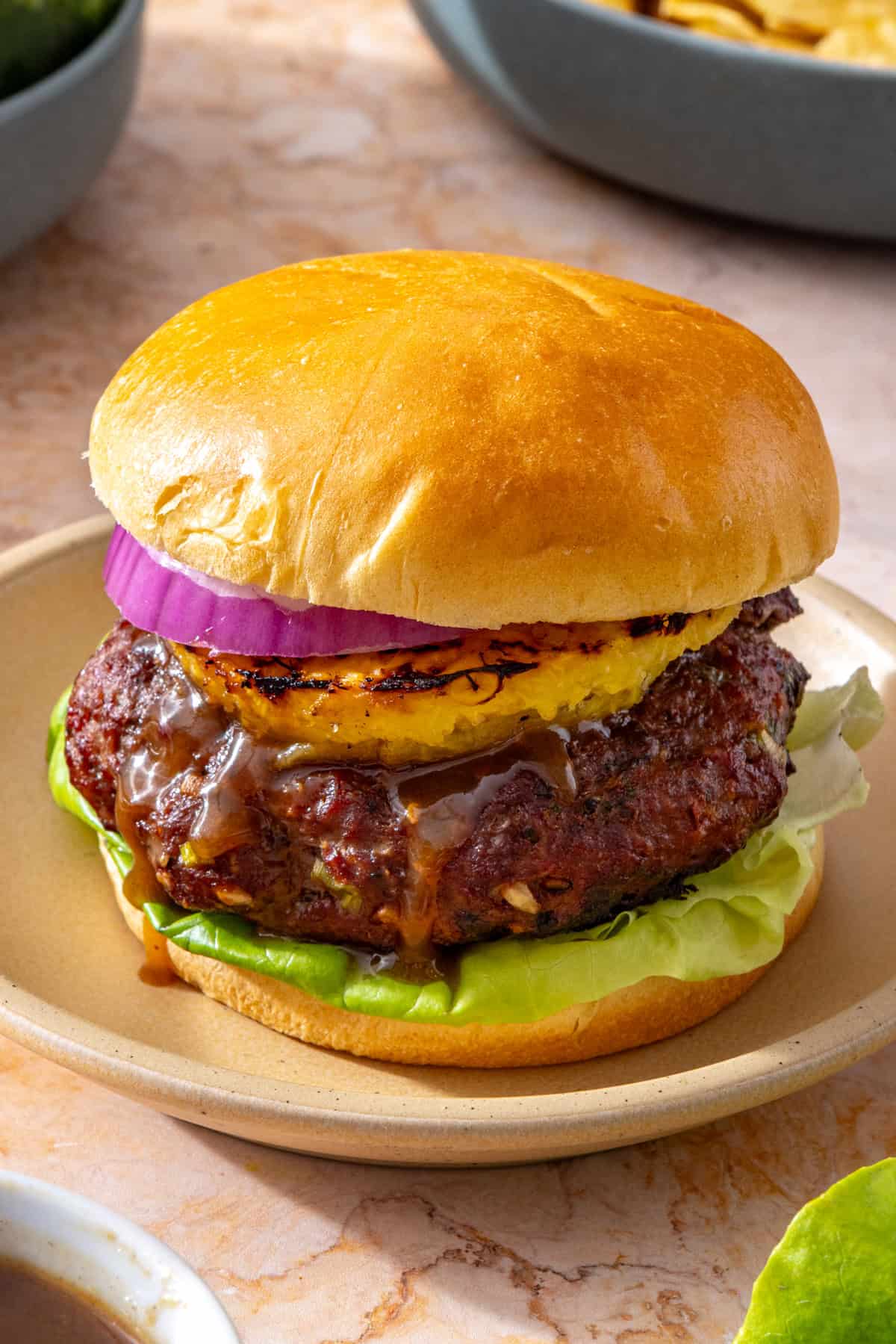 Juicy Hawaiian teriyaki burger with grilled pineapple, butter lettuce, red onion, and gluten-free brioche bun on a plate