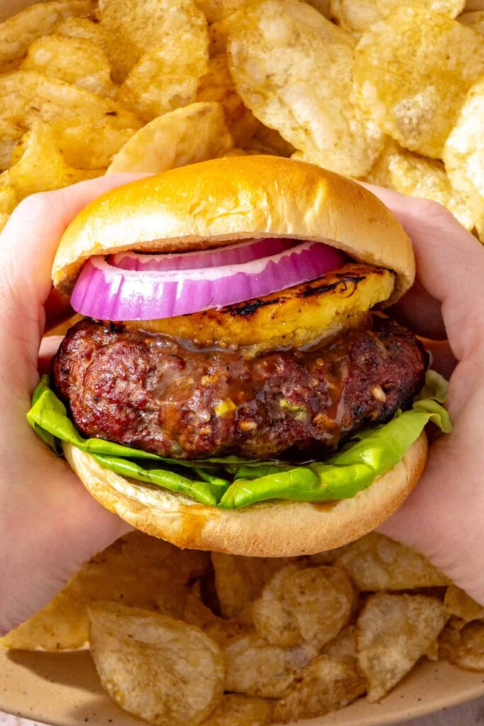 Hands holding a juicy Hawaiian teriyaki burger with grilled pineapple