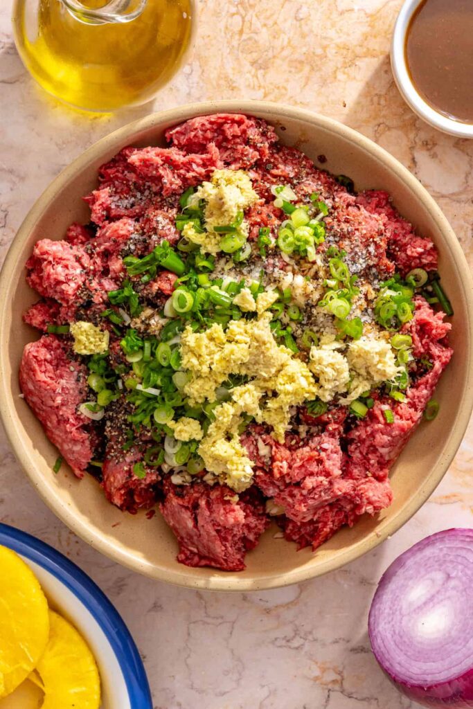 Mixing ground beef with garlic, ginger, coconut aminos, and green onions for teriyaki burgers