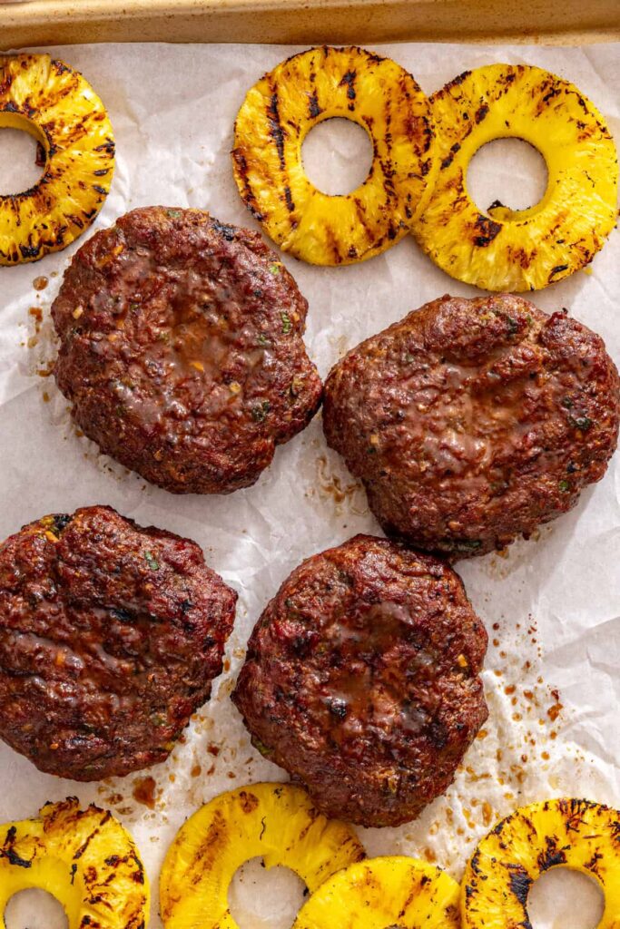 grilled homemade teriyaki burgers and fresh pineapple slices on a parchment paper-lined tray, ready to serve