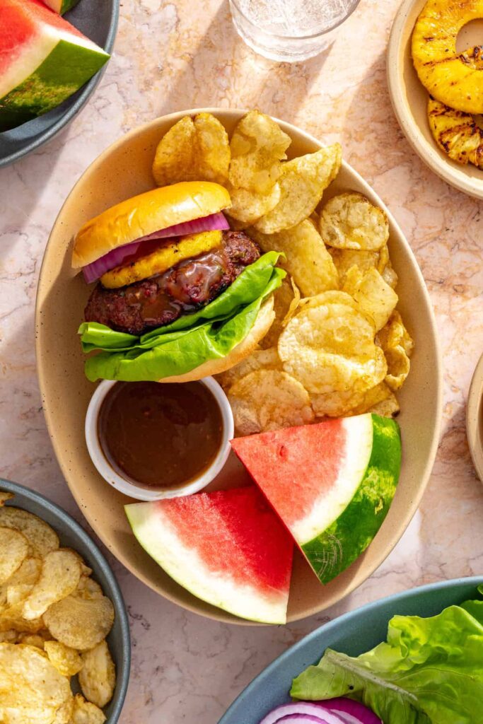 Hawaiian teriyaki burger served with chips, watermelon, and extra teriyaki sauce