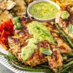 Lemon pesto grilled chicken served with grilled zucchini, asparagus, and bell peppers on a white serving platter, topped with homemade pesto and fresh lemon