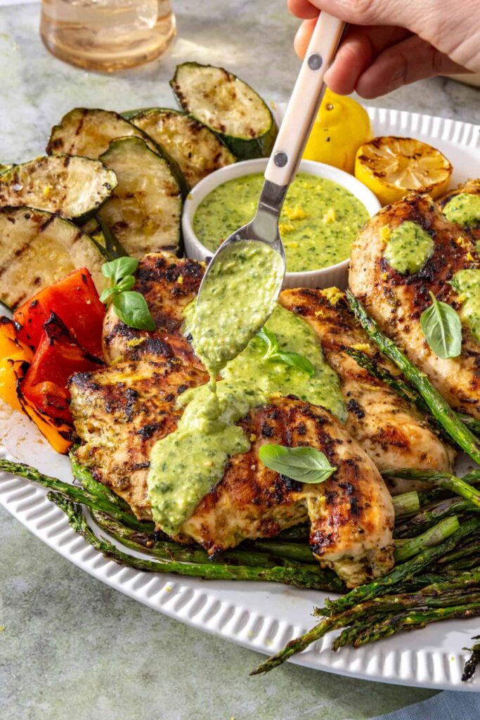 Fresh basil pesto being spooned over grilled chicken on a serving platter