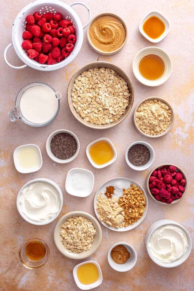 Ingredients for peanut butter and jelly overnight oats including oats, Greek yogurt, raspberries, chia seeds, peanut butter, PB2, and maple syrup